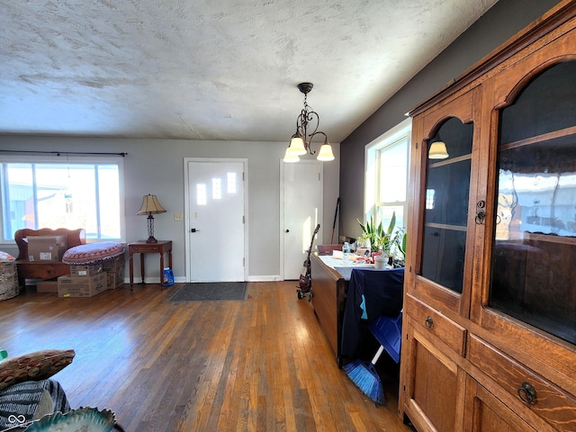 foyer entrance with a wealth of natural light, a notable chandelier, dark wood-type flooring, and baseboards