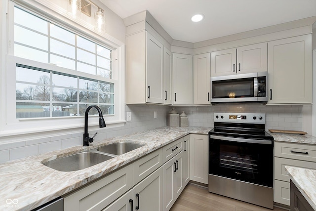 kitchen with white cabinetry, sink, stainless steel appliances, and light stone countertops