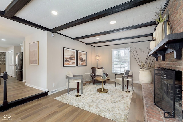 living area with beam ceiling, wood-type flooring, and a fireplace