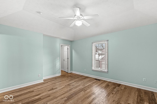 unfurnished room with vaulted ceiling, a textured ceiling, a raised ceiling, ceiling fan, and hardwood / wood-style floors