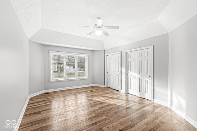 unfurnished bedroom with wood-type flooring, lofted ceiling, two closets, and ceiling fan