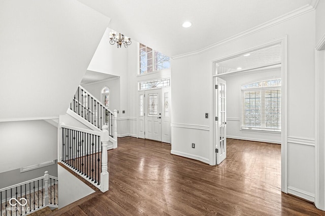 entryway with crown molding, dark wood-type flooring, and an inviting chandelier