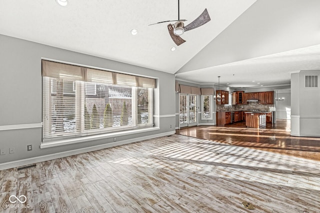 unfurnished living room with ceiling fan with notable chandelier, high vaulted ceiling, and light wood-type flooring