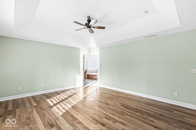 empty room with a tray ceiling, wood-type flooring, a textured ceiling, and ceiling fan