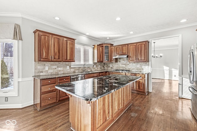 kitchen with sink, crown molding, dark stone countertops, stainless steel appliances, and a center island