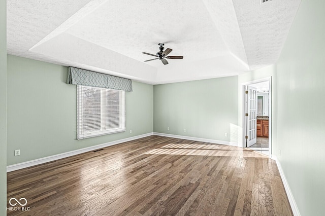 unfurnished room with ceiling fan, dark wood-type flooring, a raised ceiling, and a textured ceiling