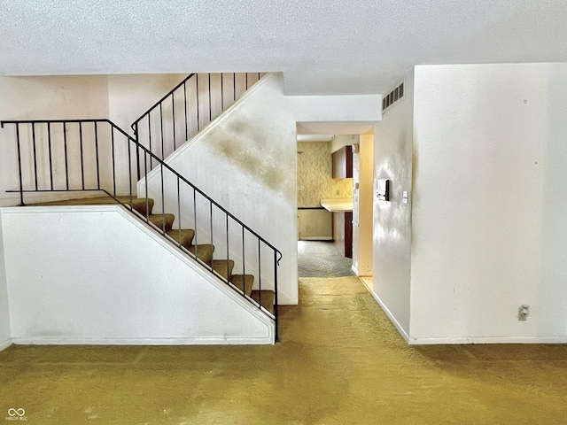 stairs with carpet floors and a textured ceiling