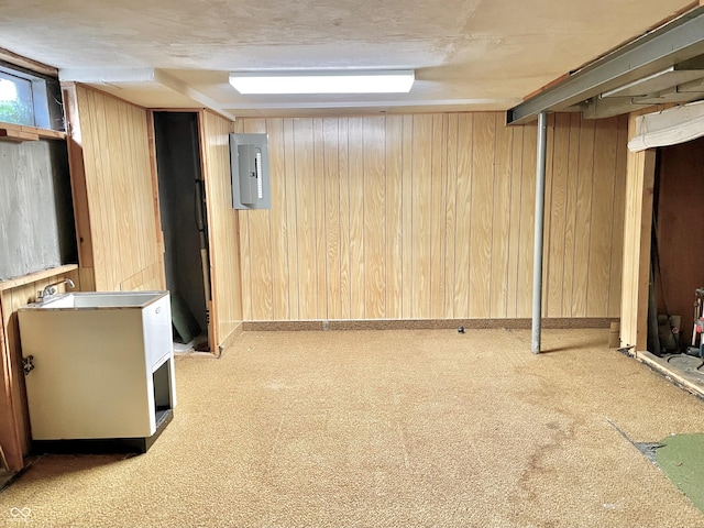 basement featuring electric panel, sink, and wood walls