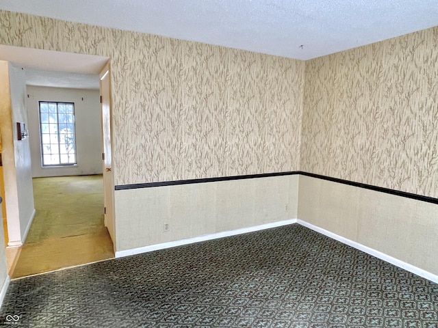 spare room with a textured ceiling and dark colored carpet