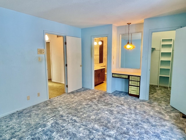 unfurnished bedroom with connected bathroom, built in desk, carpet floors, a spacious closet, and a textured ceiling