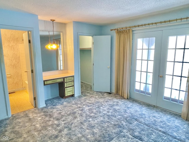 unfurnished bedroom featuring multiple windows, a walk in closet, a textured ceiling, and french doors