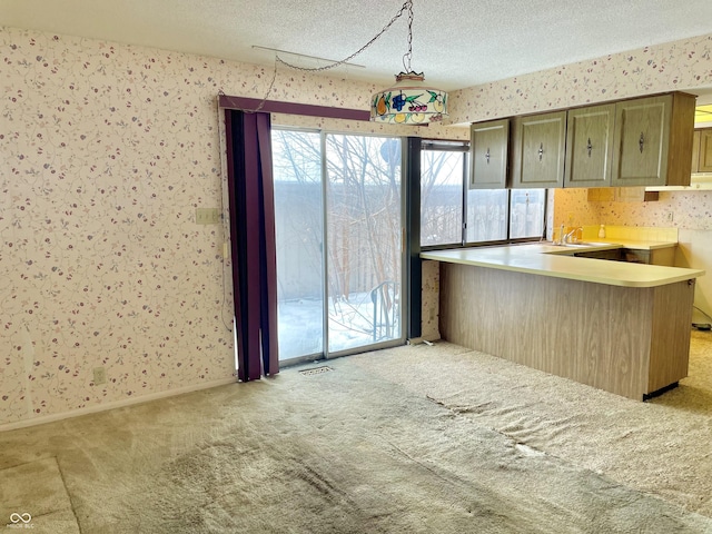 kitchen featuring sink, hanging light fixtures, a textured ceiling, light carpet, and kitchen peninsula