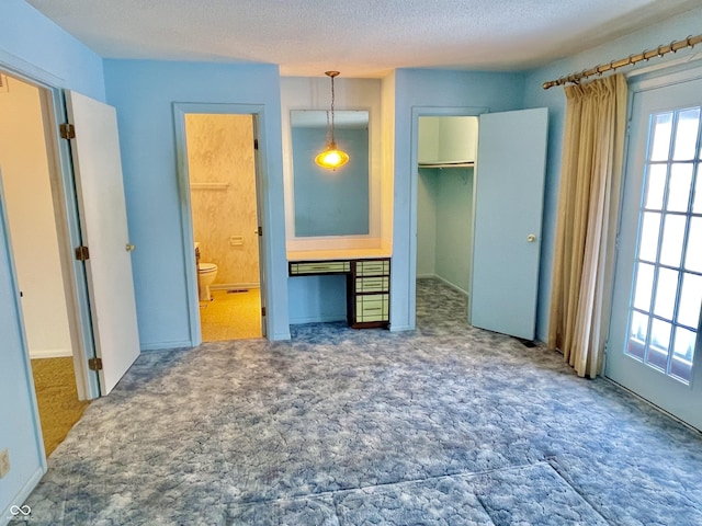 unfurnished bedroom with connected bathroom, a walk in closet, carpet, a textured ceiling, and a closet