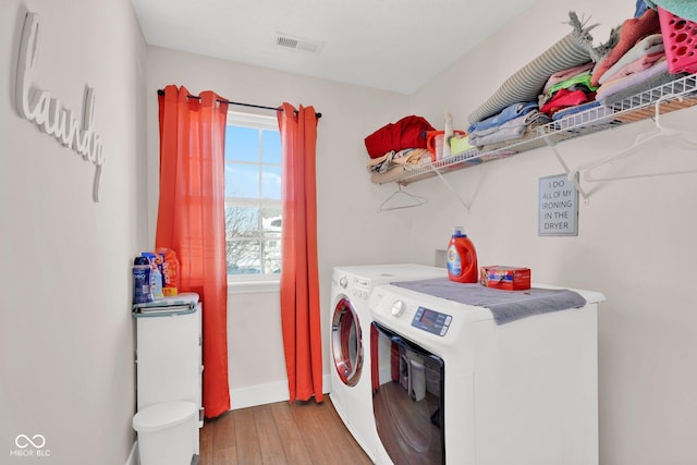 clothes washing area with wood-type flooring, separate washer and dryer, and a wealth of natural light