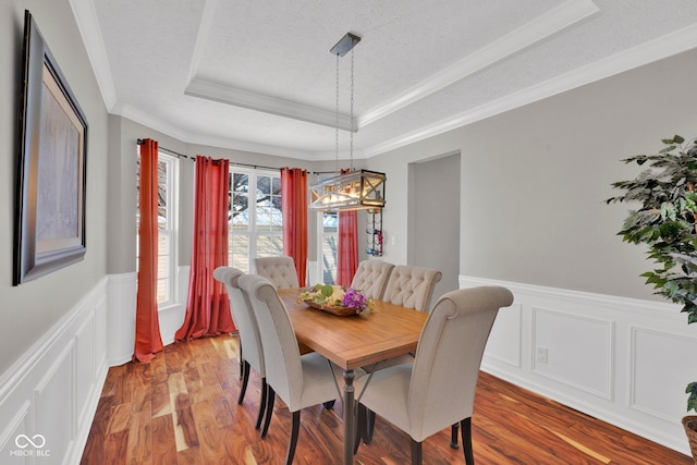 dining room featuring a textured ceiling, hardwood / wood-style flooring, ornamental molding, and a raised ceiling