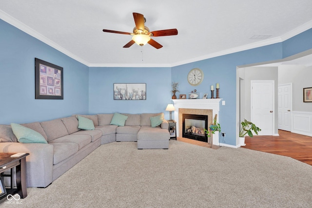 living room featuring ceiling fan, ornamental molding, a fireplace, and carpet flooring