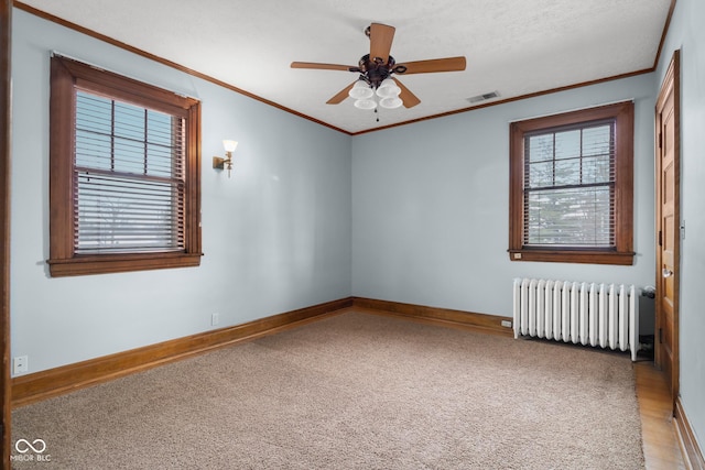 carpeted empty room featuring ceiling fan, ornamental molding, and radiator heating unit