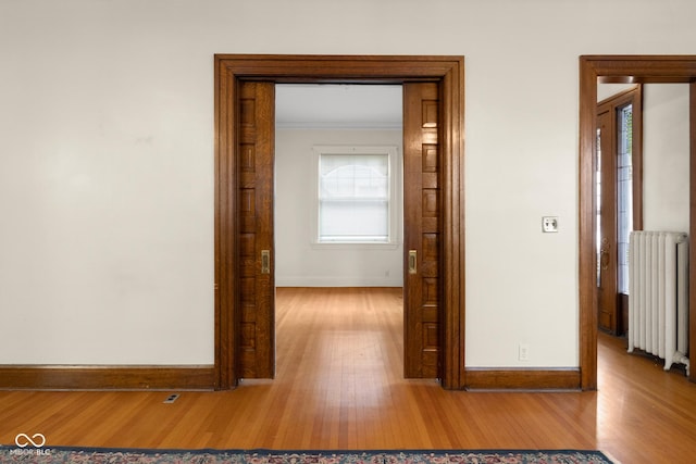 hall with crown molding, light wood-type flooring, and radiator heating unit