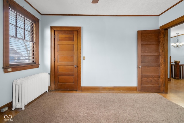 carpeted spare room with a textured ceiling, radiator, crown molding, and a notable chandelier