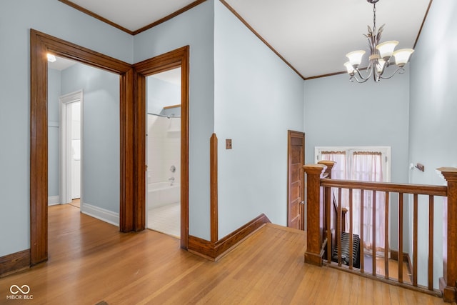 hall with light wood-type flooring, a notable chandelier, and ornamental molding