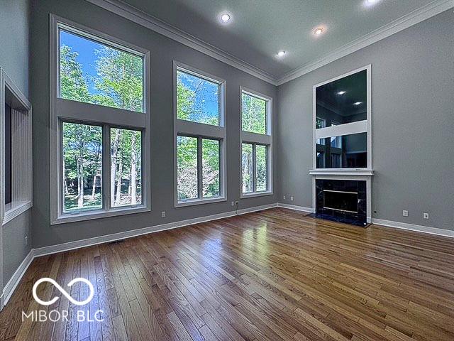 13650 Golden Ridge Ln, Fishers, IN 46055 - unfurnished living room featuring wood-type flooring, ornamental molding, a tile fireplace, recessed lighting, and a high ceiling