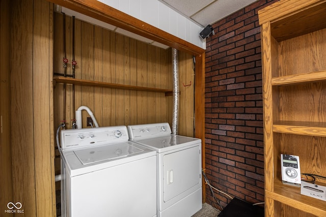 clothes washing area featuring brick wall and independent washer and dryer