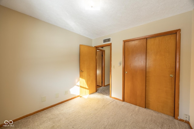 unfurnished bedroom featuring a textured ceiling, a closet, and light carpet