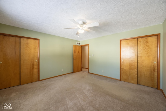 unfurnished bedroom with light carpet, multiple closets, a textured ceiling, and ceiling fan