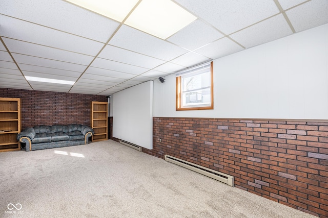 basement with brick wall, a baseboard heating unit, and a drop ceiling