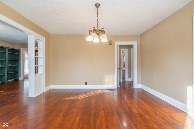 empty room with a textured ceiling, a chandelier, dark hardwood / wood-style floors, and built in shelves