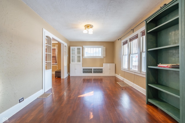 unfurnished room featuring built in features, dark hardwood / wood-style floors, and a textured ceiling