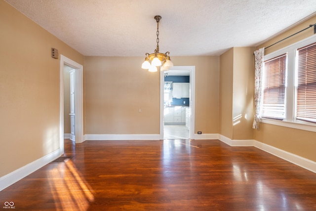 unfurnished room featuring a textured ceiling, dark wood-type flooring, and an inviting chandelier