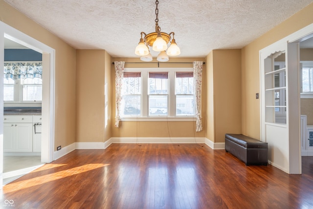 unfurnished dining area with a textured ceiling, dark wood-type flooring, and a notable chandelier