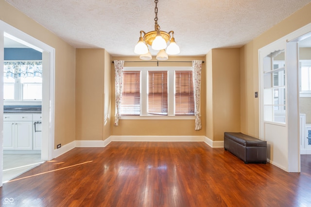 unfurnished dining area featuring a notable chandelier, a wealth of natural light, a textured ceiling, and dark hardwood / wood-style floors