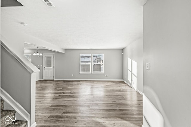 unfurnished living room featuring dark wood-type flooring, a textured ceiling, and a notable chandelier