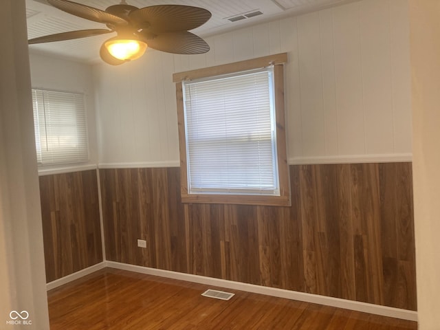 unfurnished room with wood walls, ceiling fan, and wood-type flooring