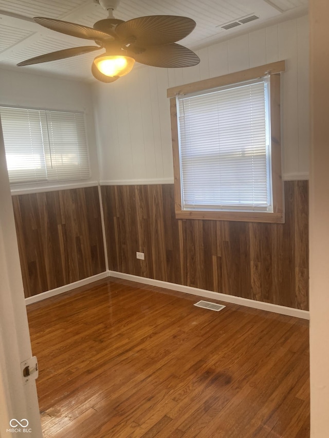 empty room featuring ceiling fan, wood-type flooring, and wood walls