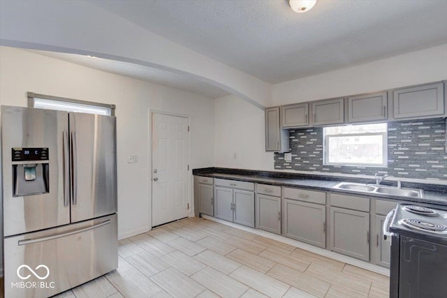 kitchen with tasteful backsplash, stainless steel refrigerator with ice dispenser, sink, black range with electric cooktop, and gray cabinetry