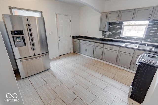 kitchen with electric range oven, tasteful backsplash, sink, stainless steel fridge, and gray cabinets