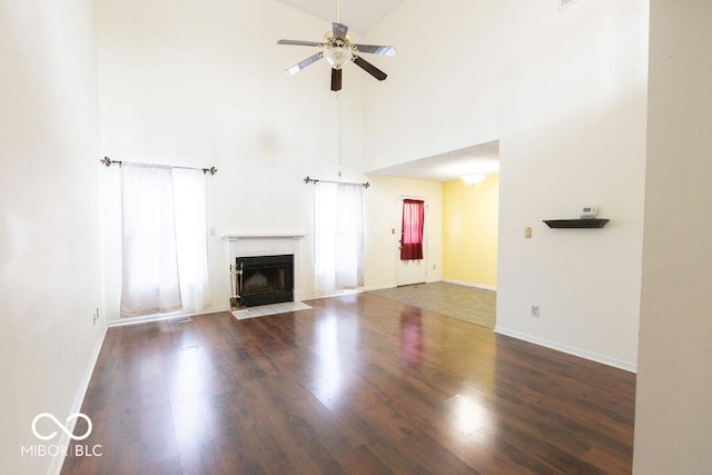 unfurnished living room with a tile fireplace, dark wood-type flooring, ceiling fan, and high vaulted ceiling