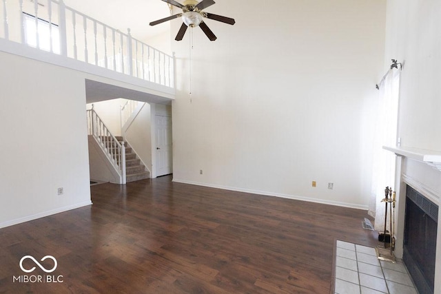 unfurnished living room with ceiling fan, dark hardwood / wood-style floors, and a high ceiling