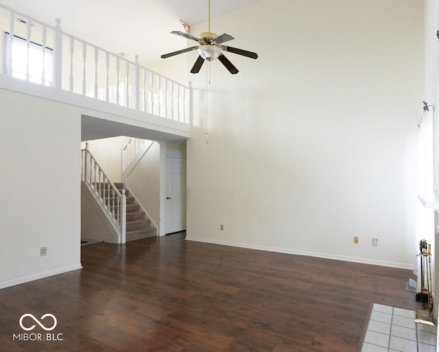 unfurnished living room with ceiling fan, a towering ceiling, and dark hardwood / wood-style floors