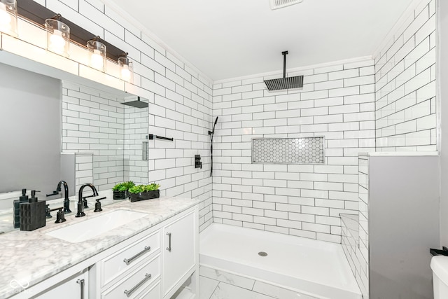 bathroom featuring a tile shower, vanity, and ornamental molding