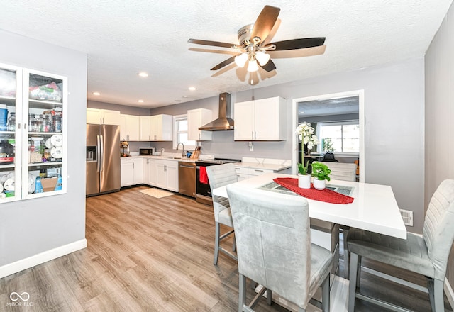 kitchen with white cabinetry, a textured ceiling, wall chimney exhaust hood, and appliances with stainless steel finishes