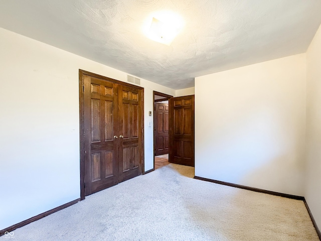 unfurnished bedroom with a closet, light colored carpet, and a textured ceiling