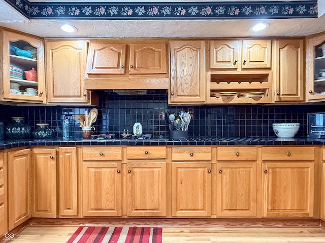 kitchen featuring light hardwood / wood-style flooring, tile counters, black gas stovetop, and tasteful backsplash