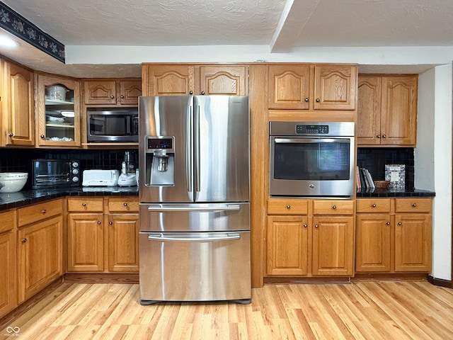 kitchen featuring light wood-type flooring, a textured ceiling, appliances with stainless steel finishes, and tasteful backsplash