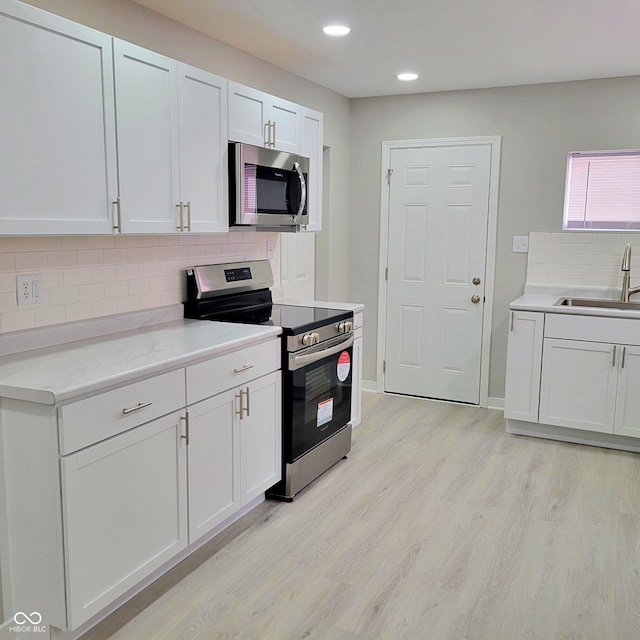 kitchen featuring sink, white cabinets, decorative backsplash, stainless steel appliances, and light hardwood / wood-style flooring