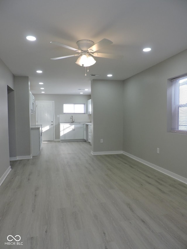 unfurnished living room with ceiling fan, sink, and light wood-type flooring