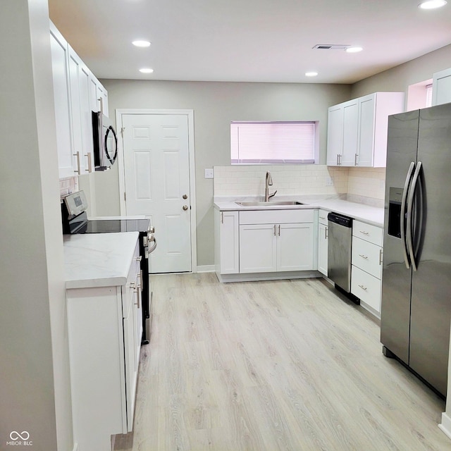 kitchen with appliances with stainless steel finishes, white cabinetry, sink, decorative backsplash, and light wood-type flooring